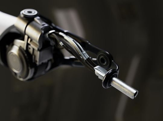 A close-up of a robotic arm with a thin metal grip at its end. The robot is made in white and black tones and is equipped with a high-precision mechanism