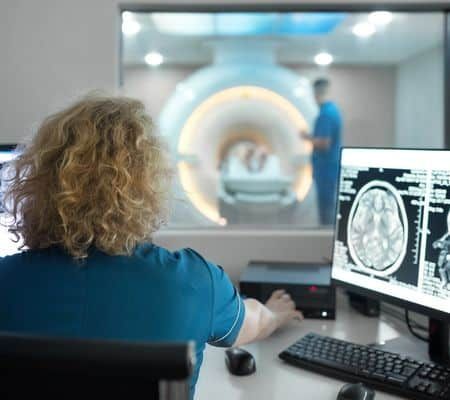 Closeup rear view of a female technicians during MRI scanning procedure discussing images in the control room.