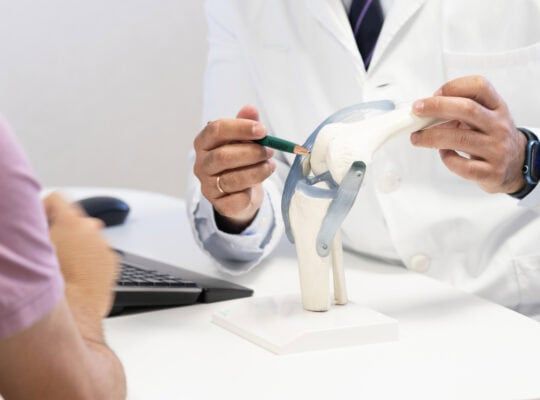 Doctor pointing at a detailed knee model to explain ligament functions to a patient, emphasizing joint health and treatment options