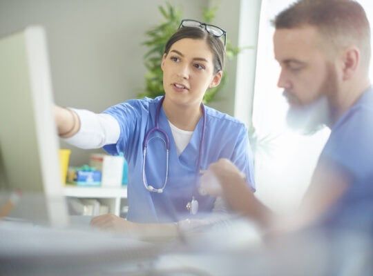 young medical professional discussing notes with her colleague at her desk .