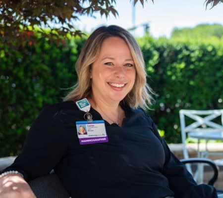 Camie Herrst, mammographer, sitting outside on bench smiling at camera