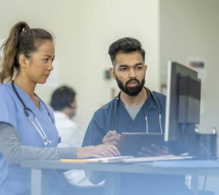 Two young adults wearing scrubs learn from their supervisor in medical school.