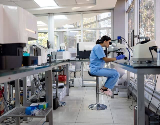 Pathologist looking at medical samples under the microscope at the laboratory – healthcare and medicine concepts