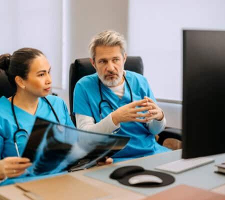 Two doctors sit at a desk analyzing a lung x ray together. Captures medical teamwork, diagnosis, and professional healthcare discussion.